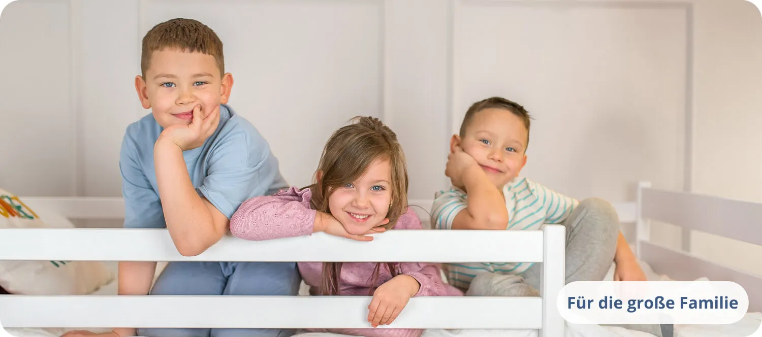 Drei lächelnde Kinder lehnen an einer weißen Bettschutzreling.